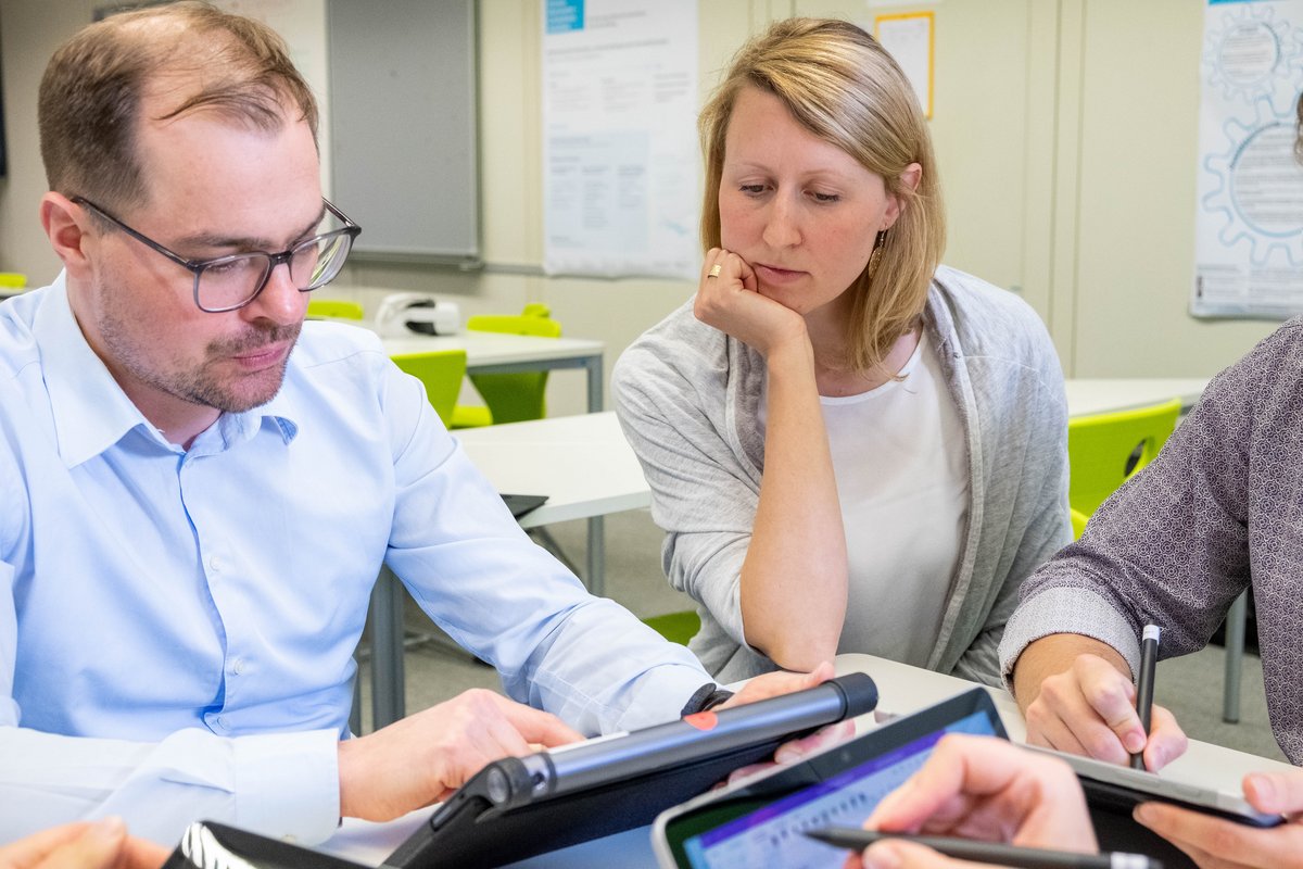 Lehrperson und Studierender schauen gemeinsam auf ein Tablet.